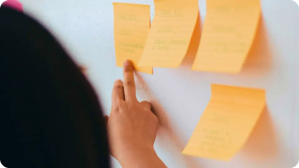 Woman from behind putting yellow post-it notes on a white wall, planning.