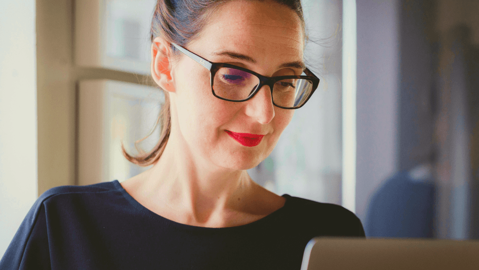 Woman with glasses in black shirt looking at her laptop screen.